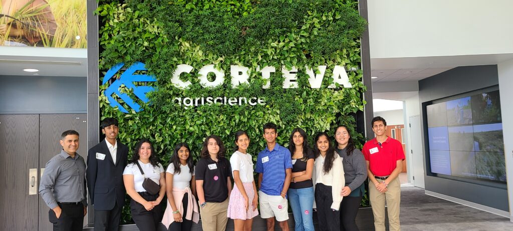 The YiQ 2023 cohort stands in front of a Corteva Agriscience sign covered in bright green leaves.